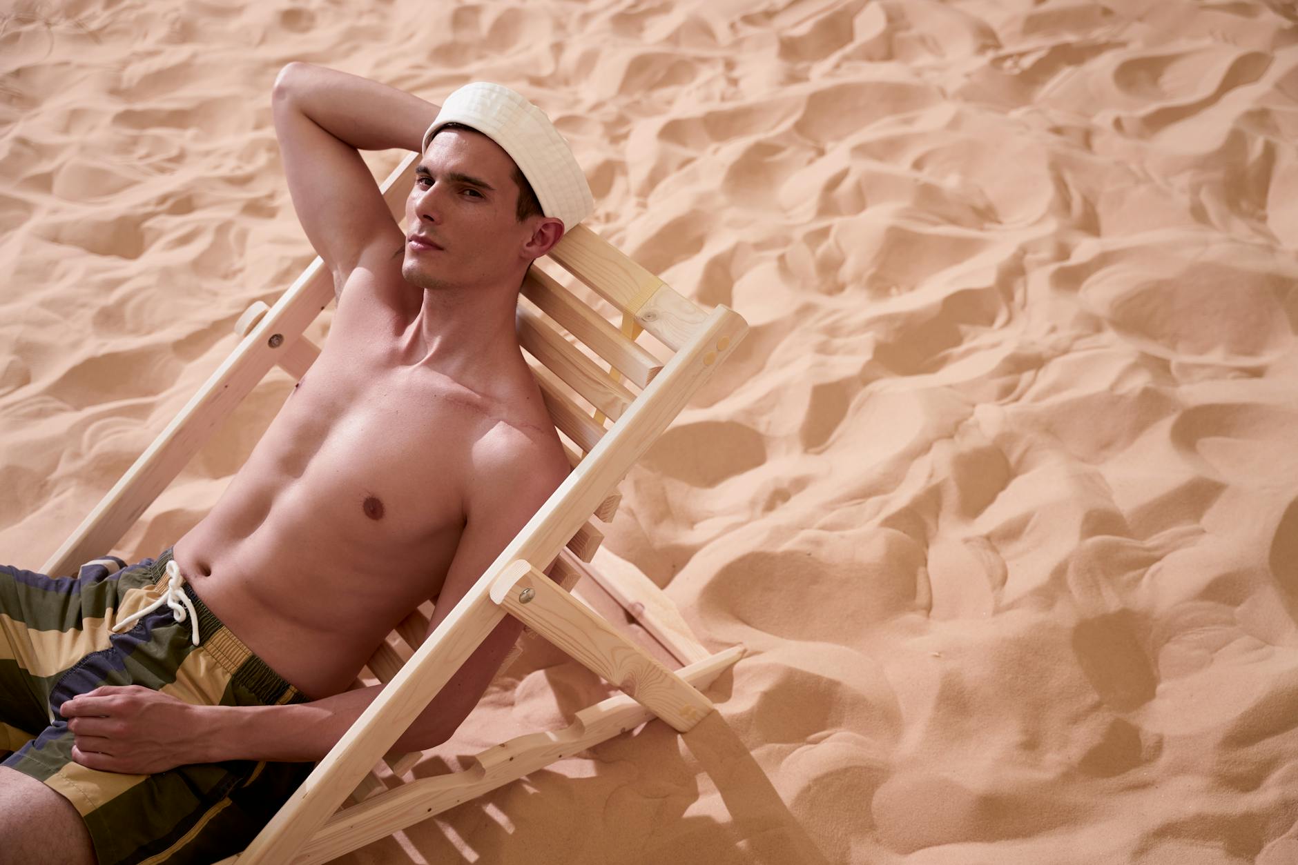 Mężczyzna bez koszulki odpoczywa na drewnianym leżaku na plaży