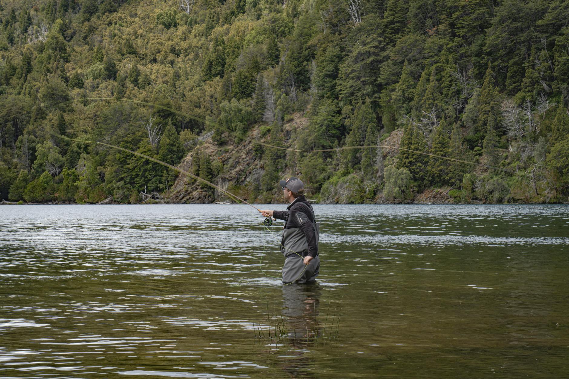 Wędkarz muchowy na tle gór i lasu nad przejrzystym jeziorem
