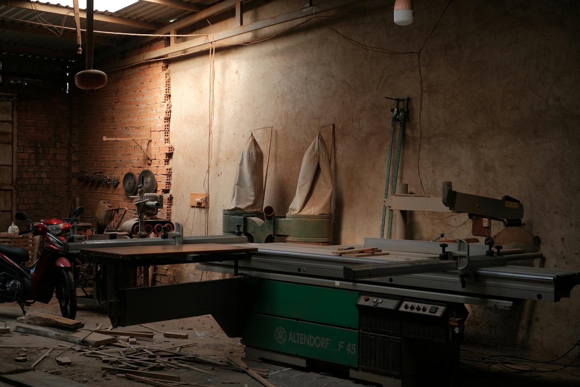 Przyciemniony warsztat z piłą Altendorf F45 i narzędziami industrialnymi