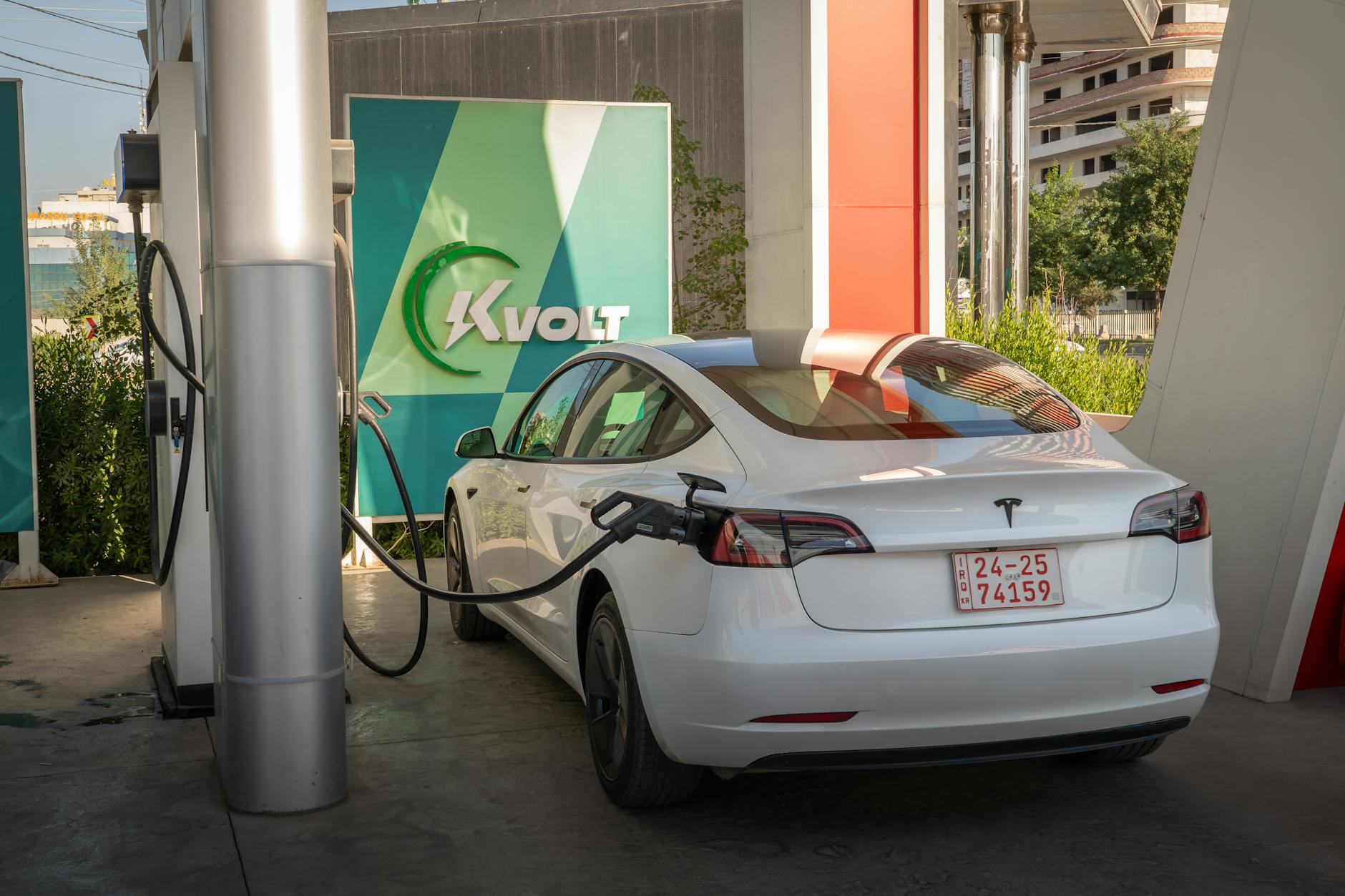 Biały Tesla Model 3 ładuje się na zewnętrznej stacji ładowania Kvolt