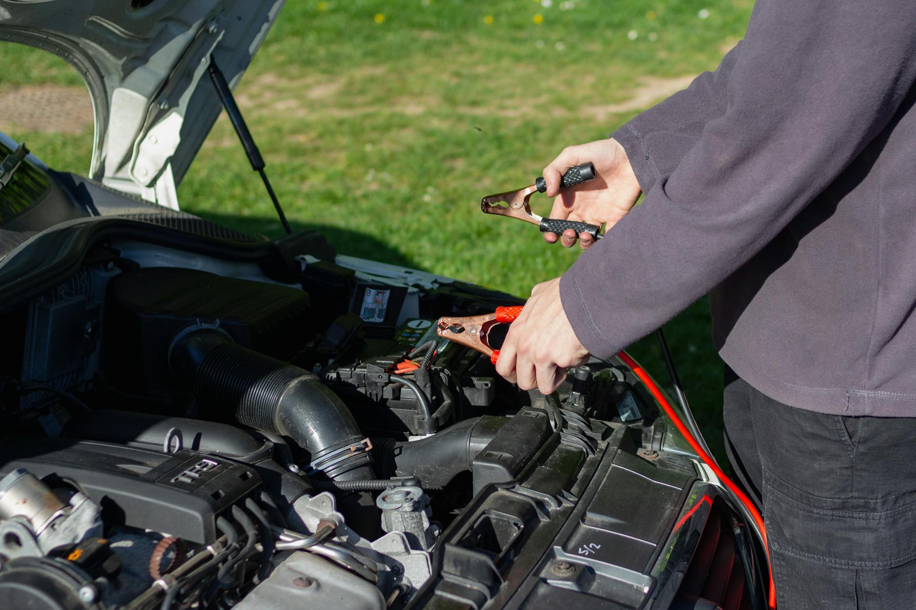 Mechanik podłącza kable rozruchowe do akumulatora samochodu na dworze