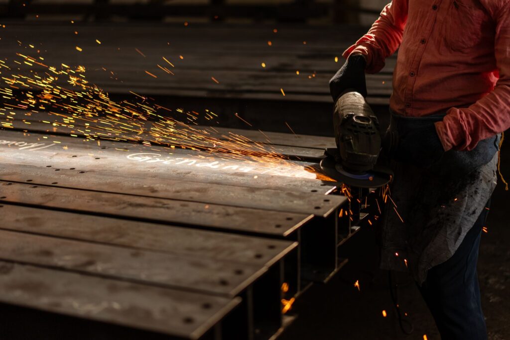 Pracownik szlifuje metalowe belki szlifierką kątową, wzbijając iskry