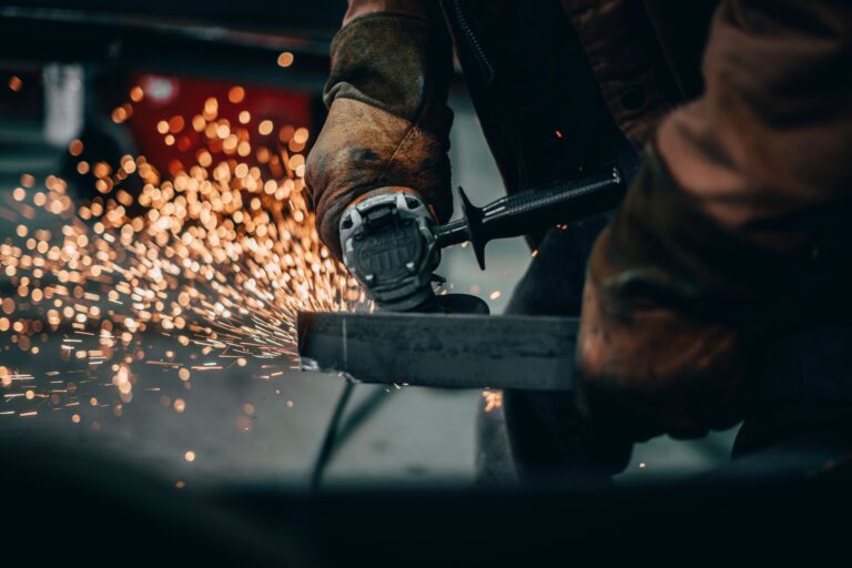Pracownik tnie metal szlifierką kątową wśród iskier w fabryce