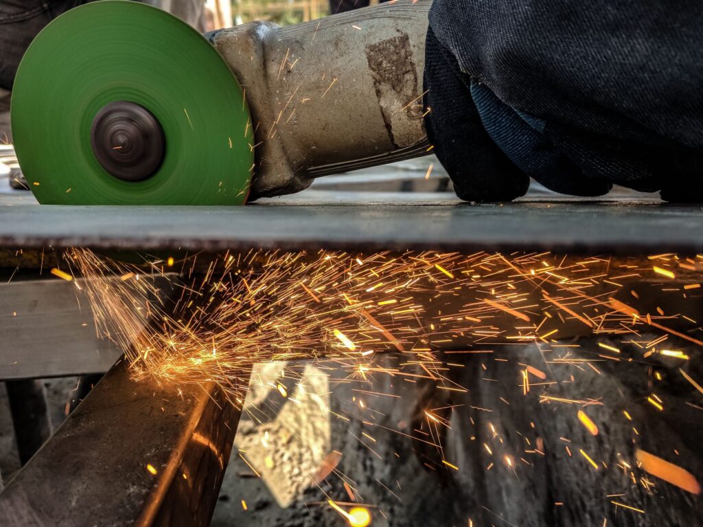 Pracownik tnie metal szlifierką, spod tarczy lecą iskry