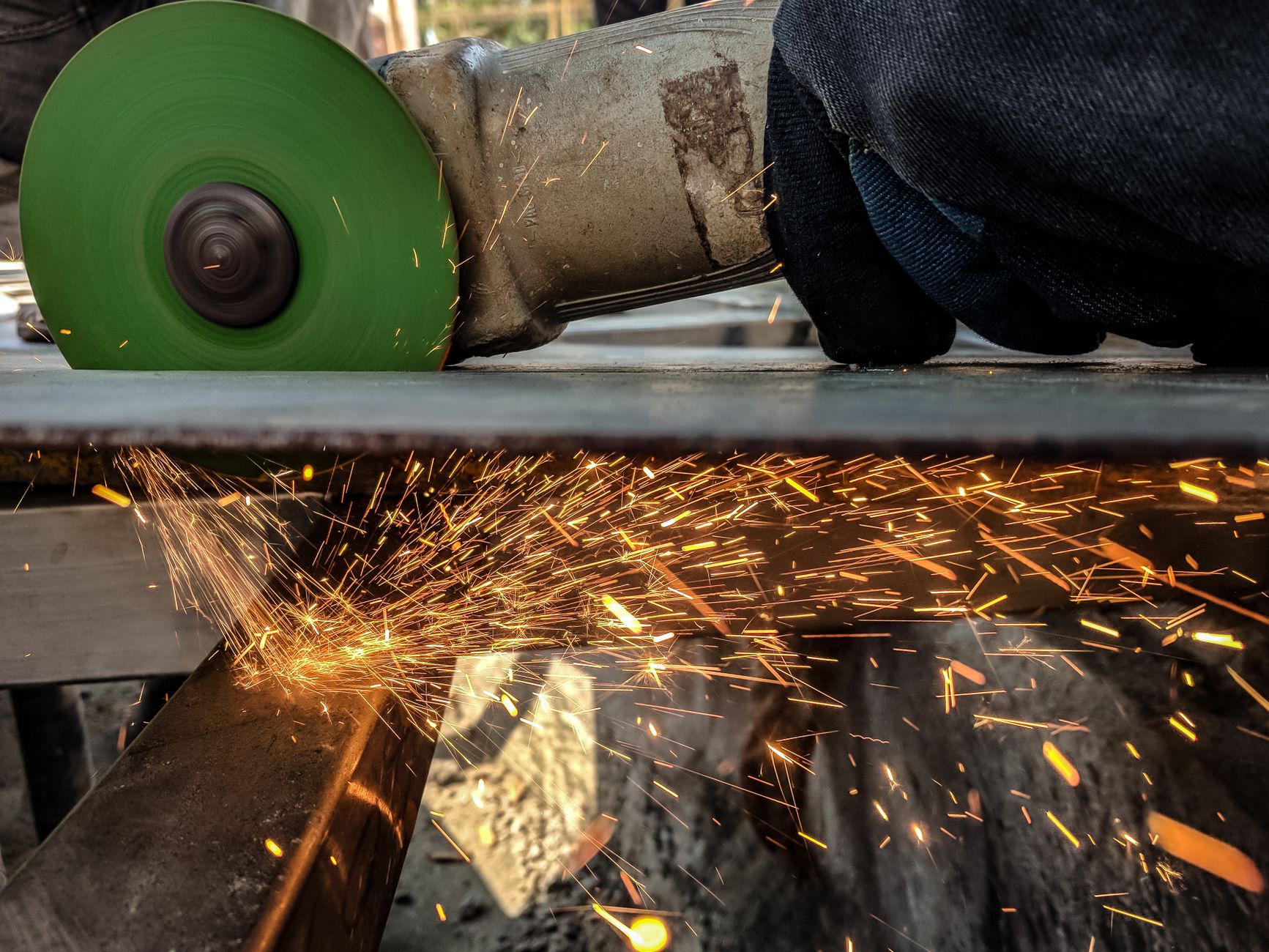 Pracownik tnie metal szlifierką, spod tarczy lecą iskry