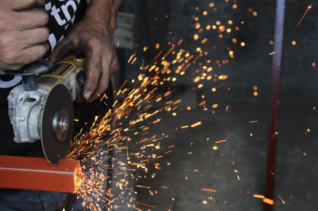 Pracownik tnie metal szlifierką, wzbijając iskry